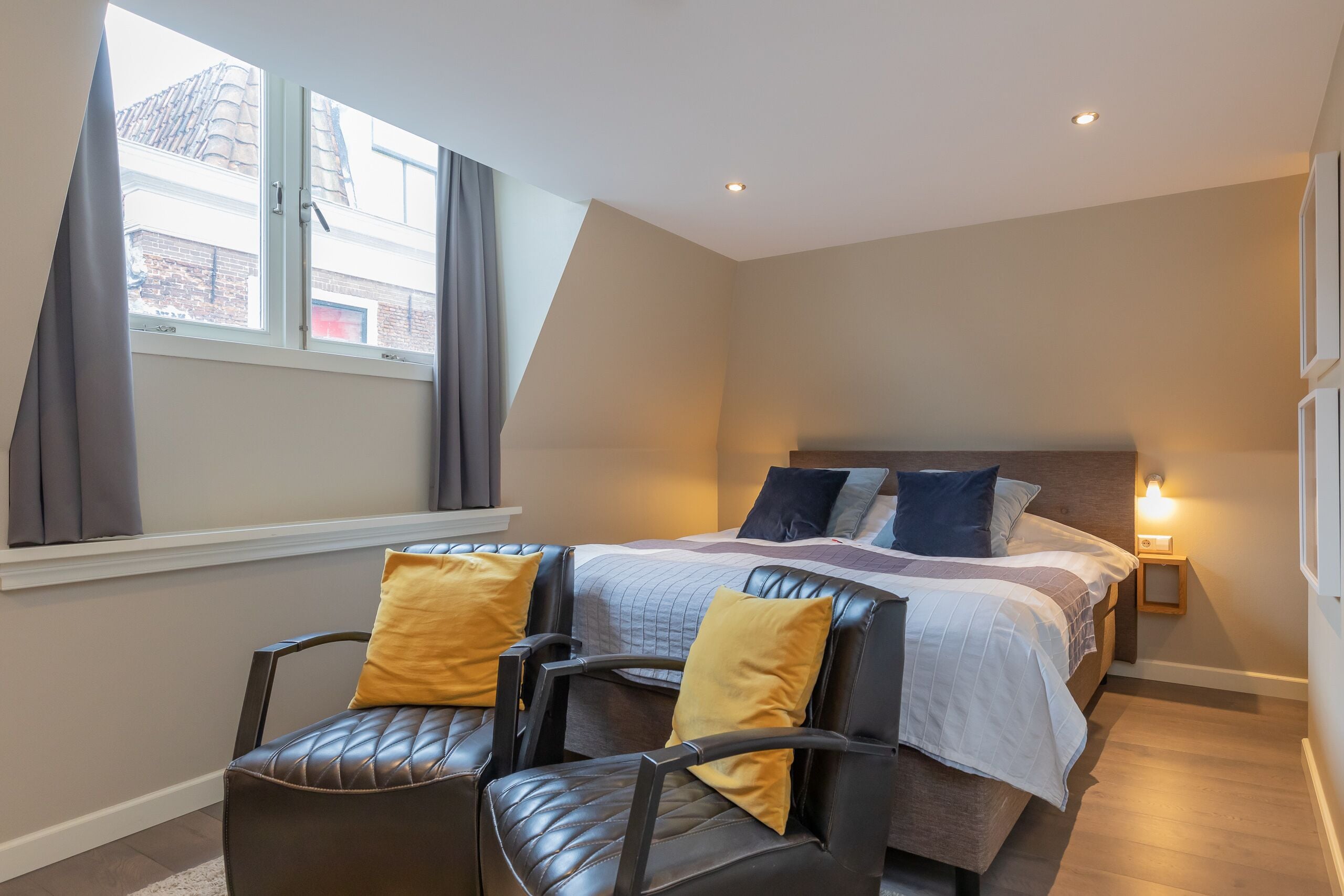 A bedroom with a bed, two chairs, a nightstand, and a window with curtains.
