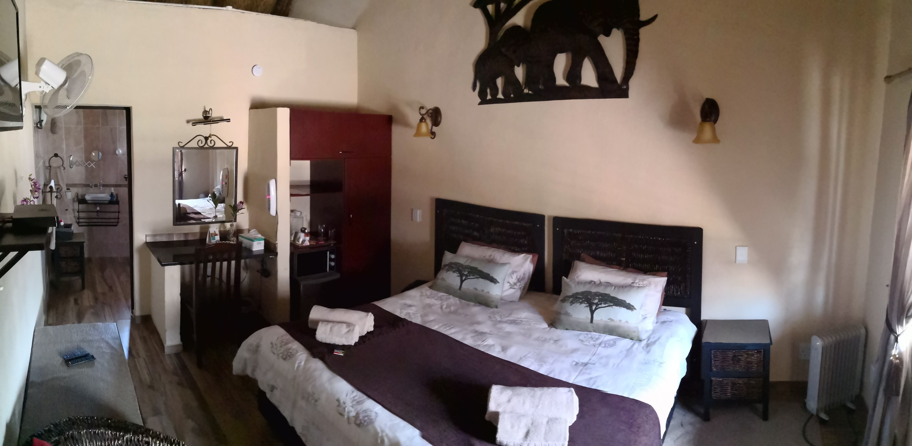 A bedroom with a large bed, a desk with a mirror, a red wardrobe, and a wall-mounted elephant decoration.