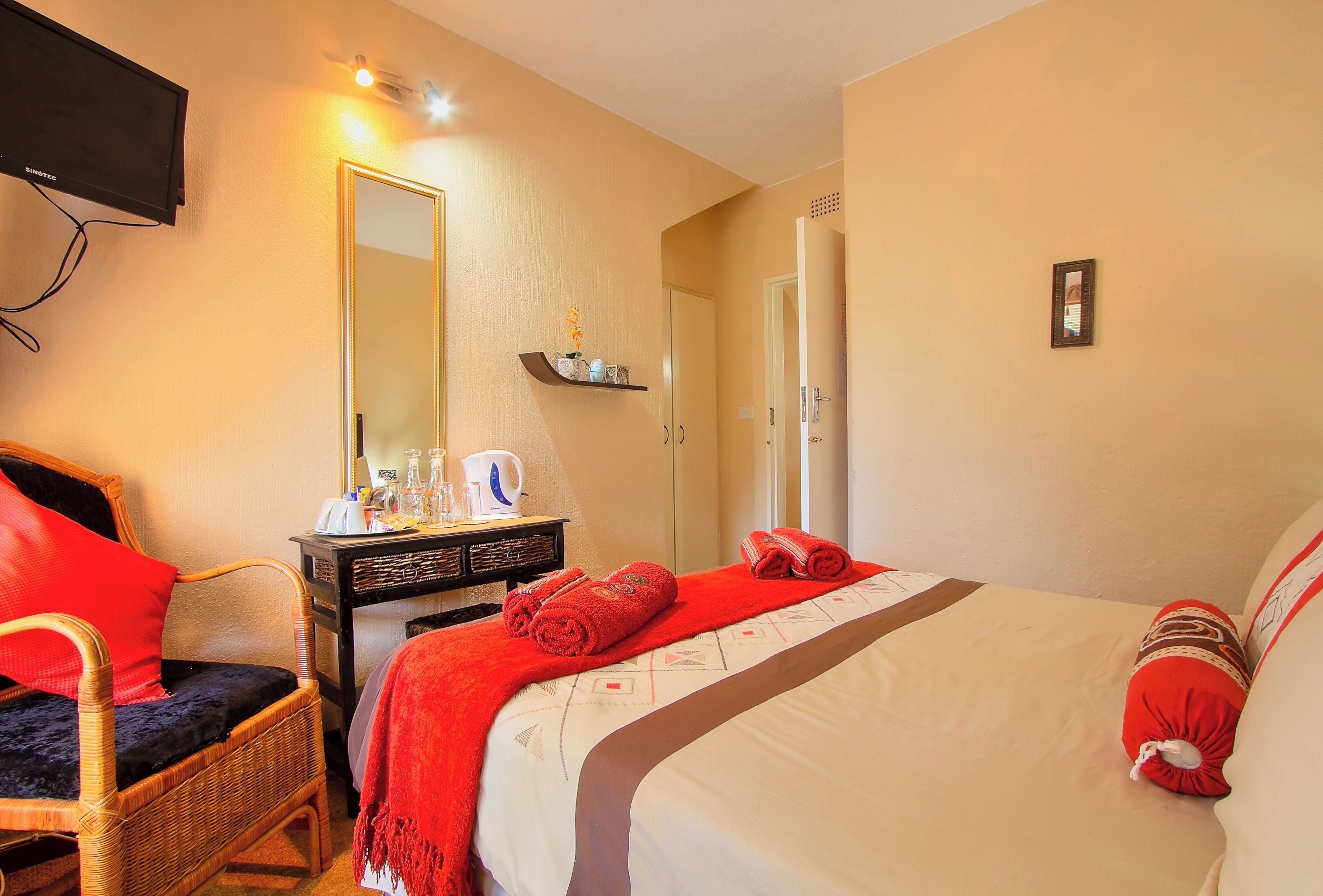 Une chambre d’hôtel comprenant un lit, une chaise, un bureau avec une bouilloire, un miroir et une étagère avec des articles de toilette.