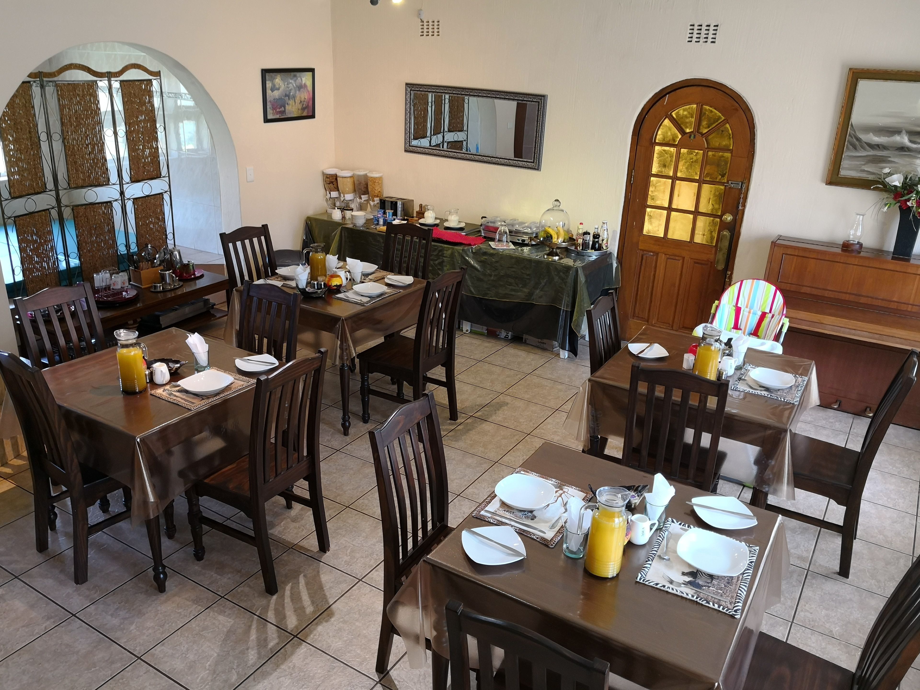 A dining area with multiple tables set for breakfast, equipped with coffee makers, juice dispensers, and breakfast items.