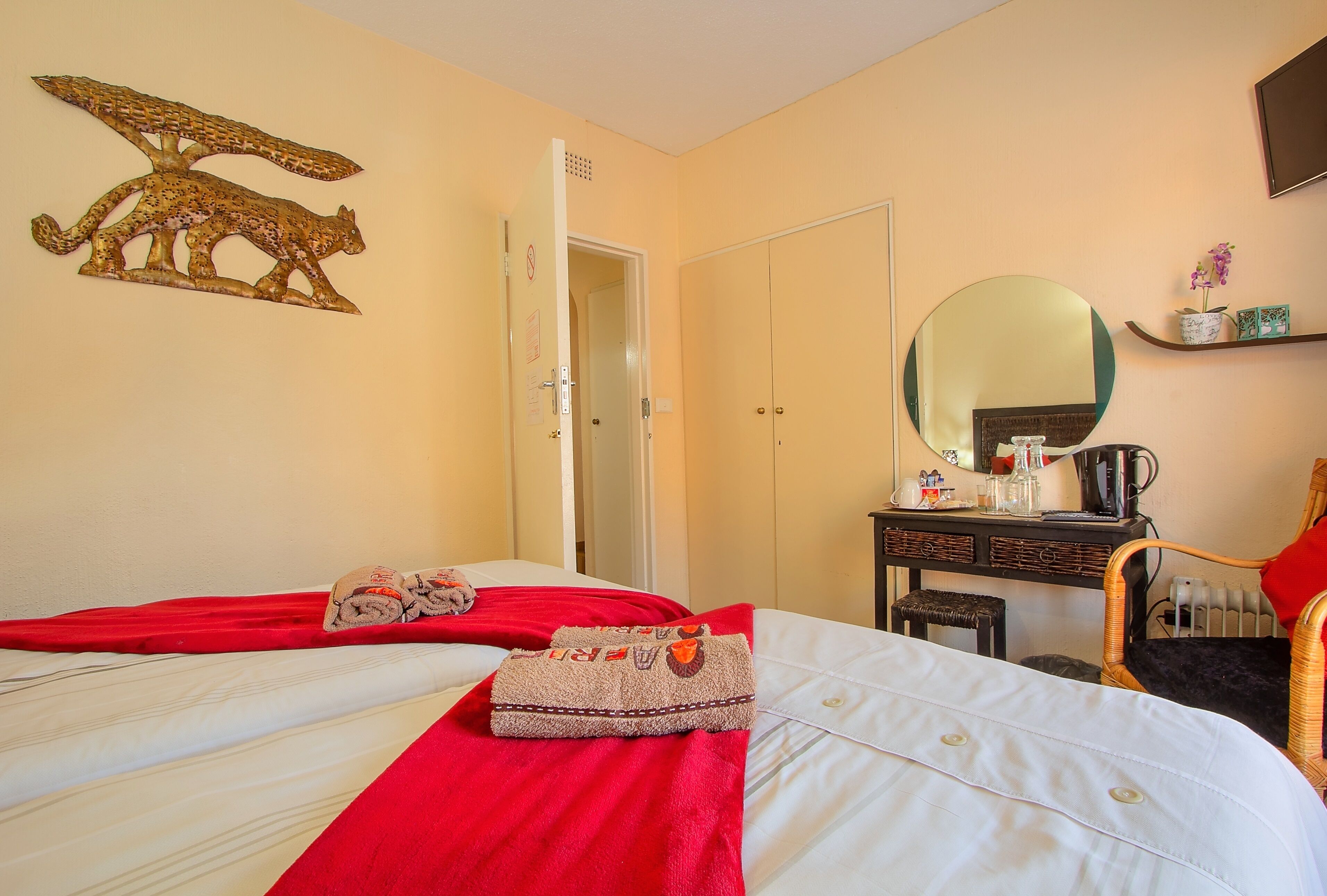 A hotel room with two beds, a red blanket, a towel, a mirror, a dresser, and a wall decoration.