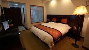 Una habitación de hotel con una cama grande, una lámpara de noche y un escritorio con una computadora.