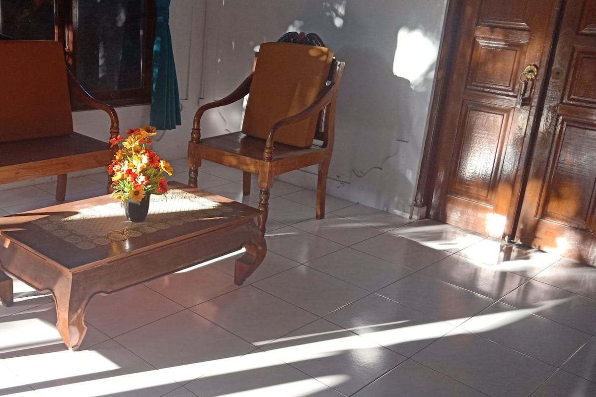 A room with a wooden sofa, a wooden chair, and a coffee table with a vase of flowers.