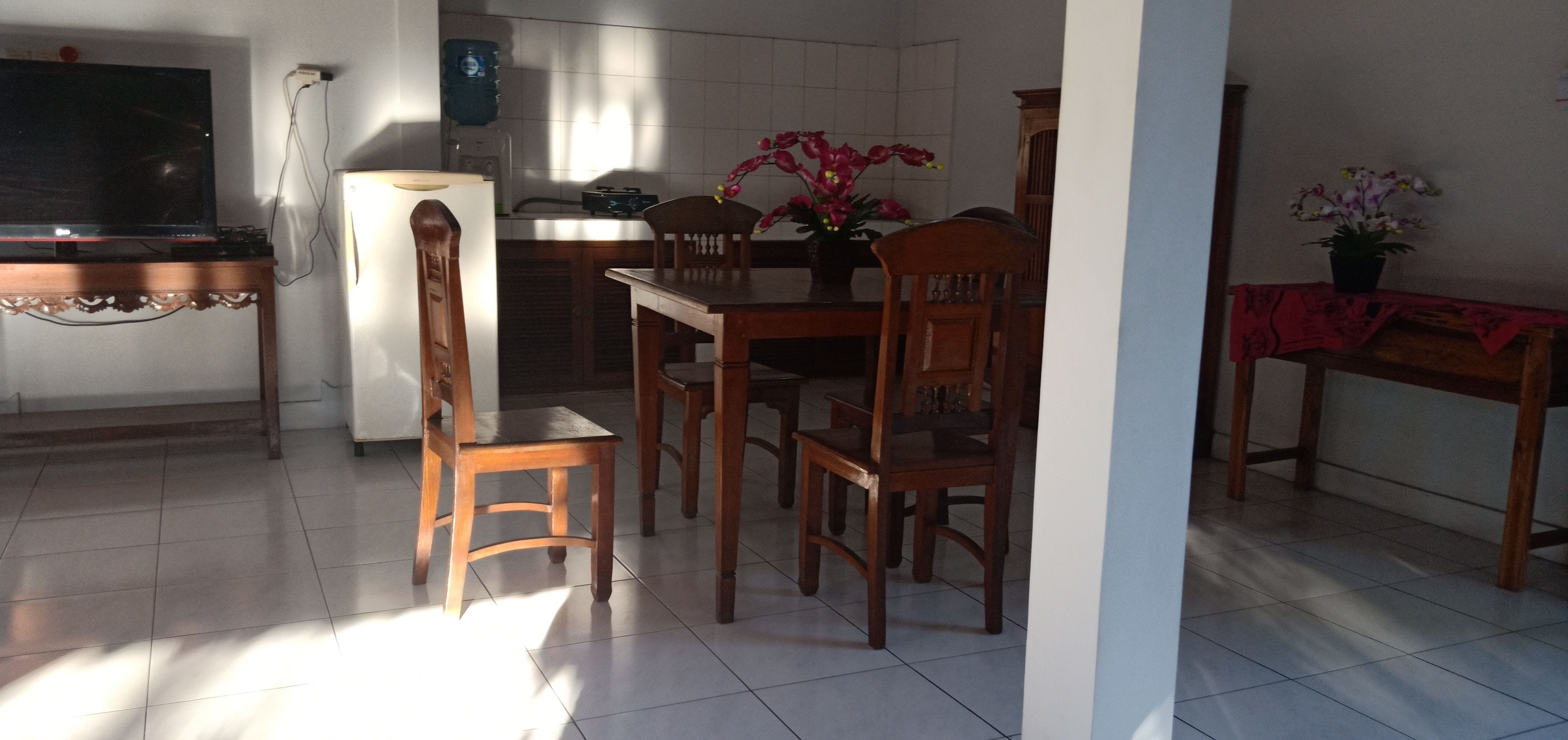 A kitchen with wooden chairs, a dining table, a refrigerator, and a water dispenser.