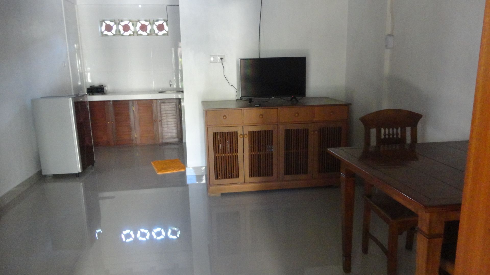 Una cocina con un refrigerador, un mueble de madera con una televisión y una mesa de comedor con una silla.