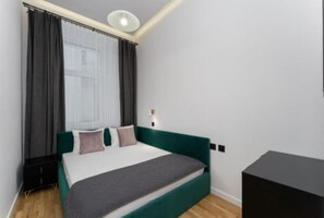 Un dormitorio con cama, cortinas, mesita de noche y una lámpara de pared.