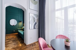Un intérieur moderne avec un parquet en chevrons, des murs d’accent de couleur turquoise, un miroir rond, un canapé turquoise, un fauteuil rose et une table agrémentée d’une plante.