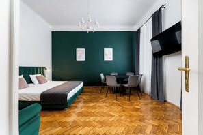 A hotel room with a bed, a dining table with chairs, a TV, and artwork on the wall.