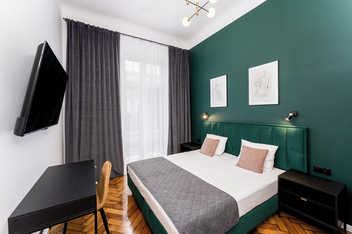 Et moderne hotelværelse med en seng, sengeborde, et skrivebord og et fjernsyn.
