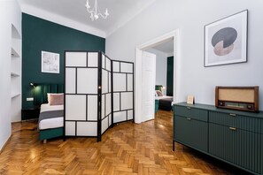 Une chambre moderne avec un parquet en bois à motifs chevrons, un lit vert, une table de chevet blanche et une cloison à cadre noir.