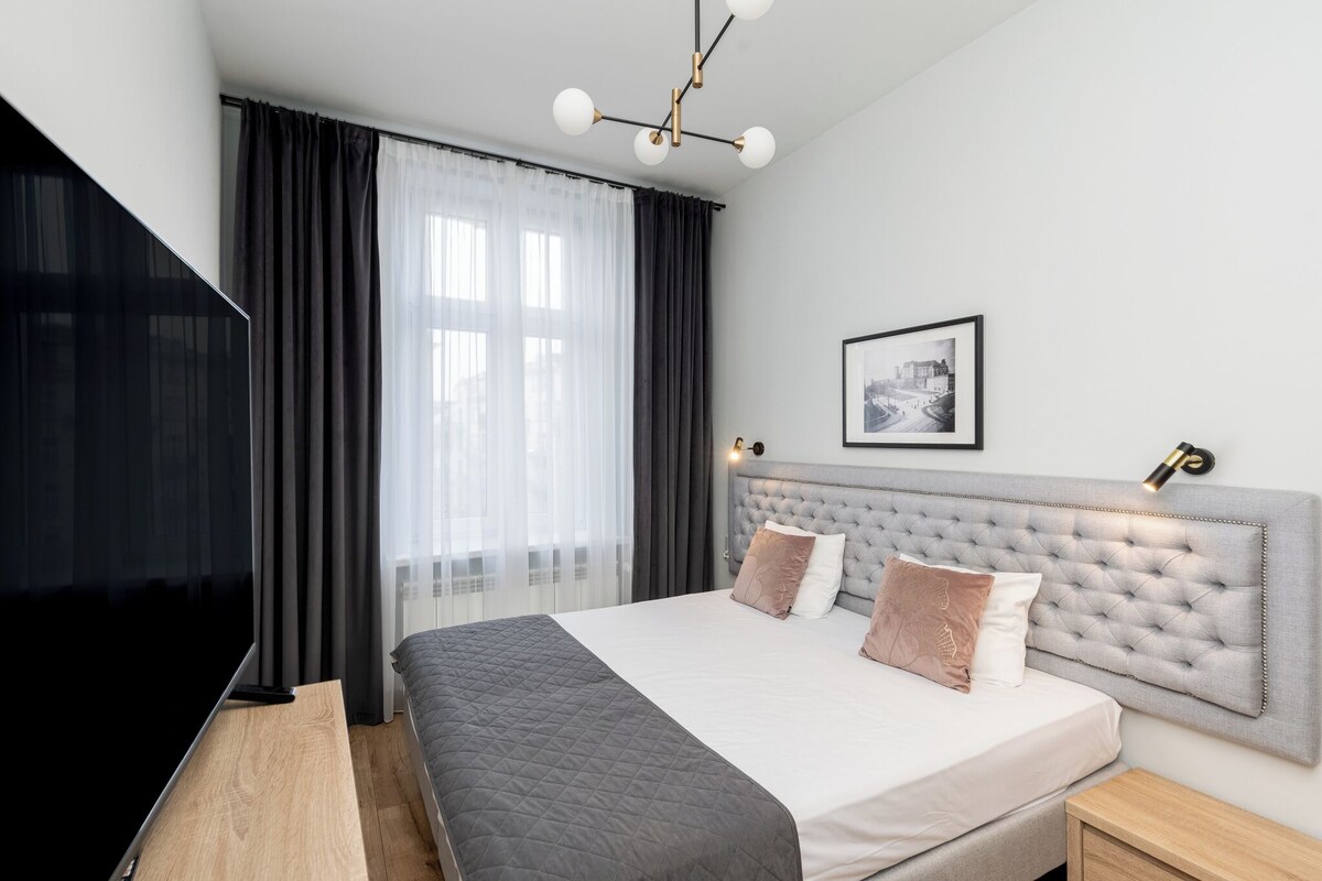 Et moderne soveværelse med en stor seng, et fladskærms-tv, et indrammet bybillede og et natbord med en lampe.