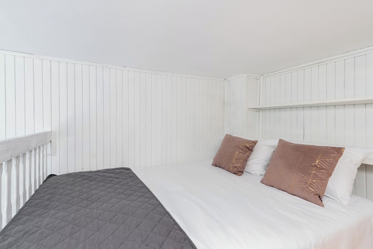 Un lit simple avec une tête de lit matelassée, deux oreillers et un mur blanc orné de panneaux verticaux.