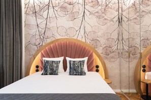 Une chambre à coucher avec un lit, deux oreillers, une tête de lit et un mur orné d’un motif de feuilles.