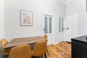 A dining area with a wooden table and two chairs, a framed artwork on the wall, and a kitchen area with white doors. - Wawel Apartments - Old Town (Kraków)