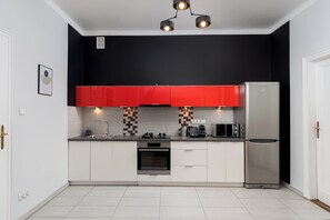 A compact kitchen with a stainless steel refrigerator, a microwave, a kettle, and a built-in oven.