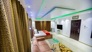 A modern hotel room with a sofa, a small table, a bed with a red blanket, and a television. - NAP APARTMENT HOTEL (Accra)