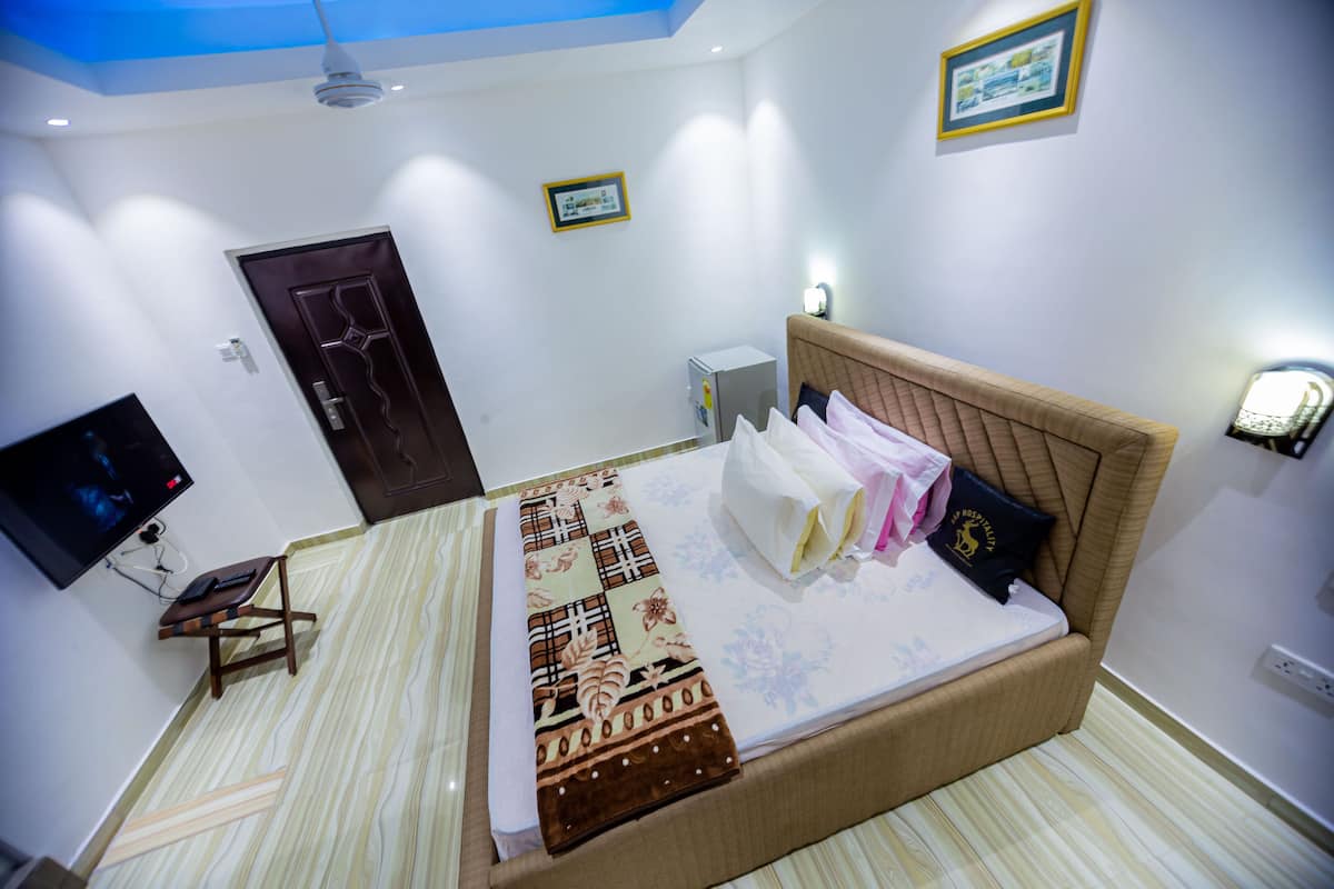 A neatly arranged bedroom with a bed, a small desk, a television, and a door.