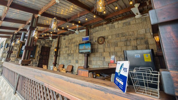 A reception area with a stone wall, wooden reception desk, and hanging pendant lights. - NAP APARTMENT HOTEL (Accra)