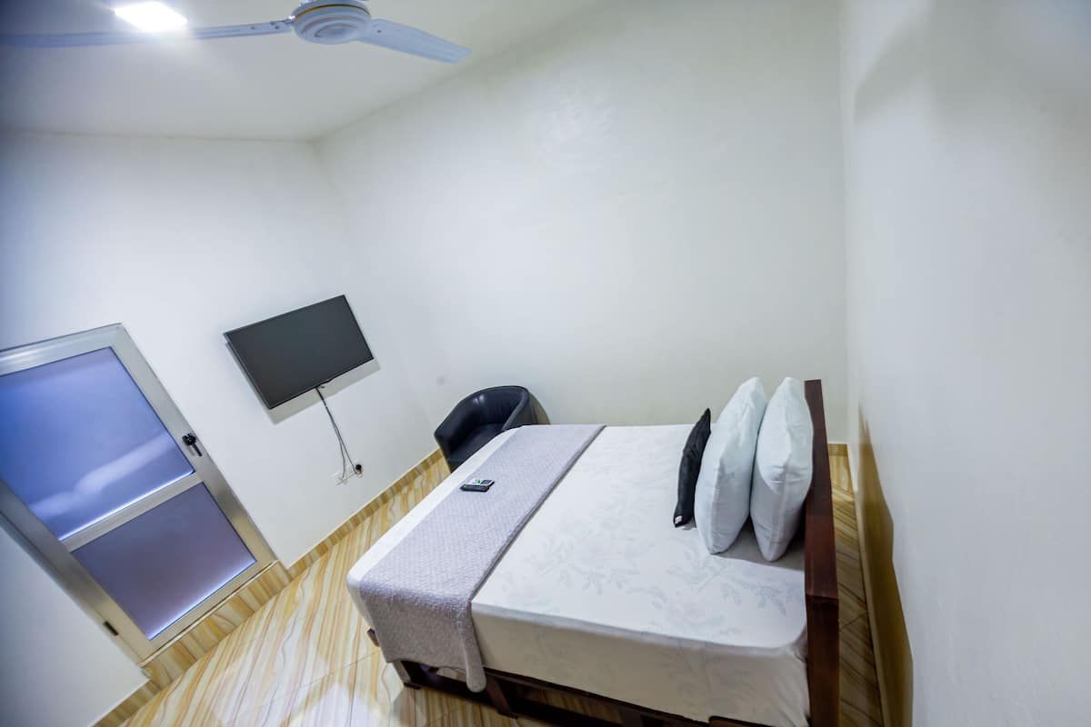 A small, clean room with a bed, a desk, a chair, a TV, and a door.