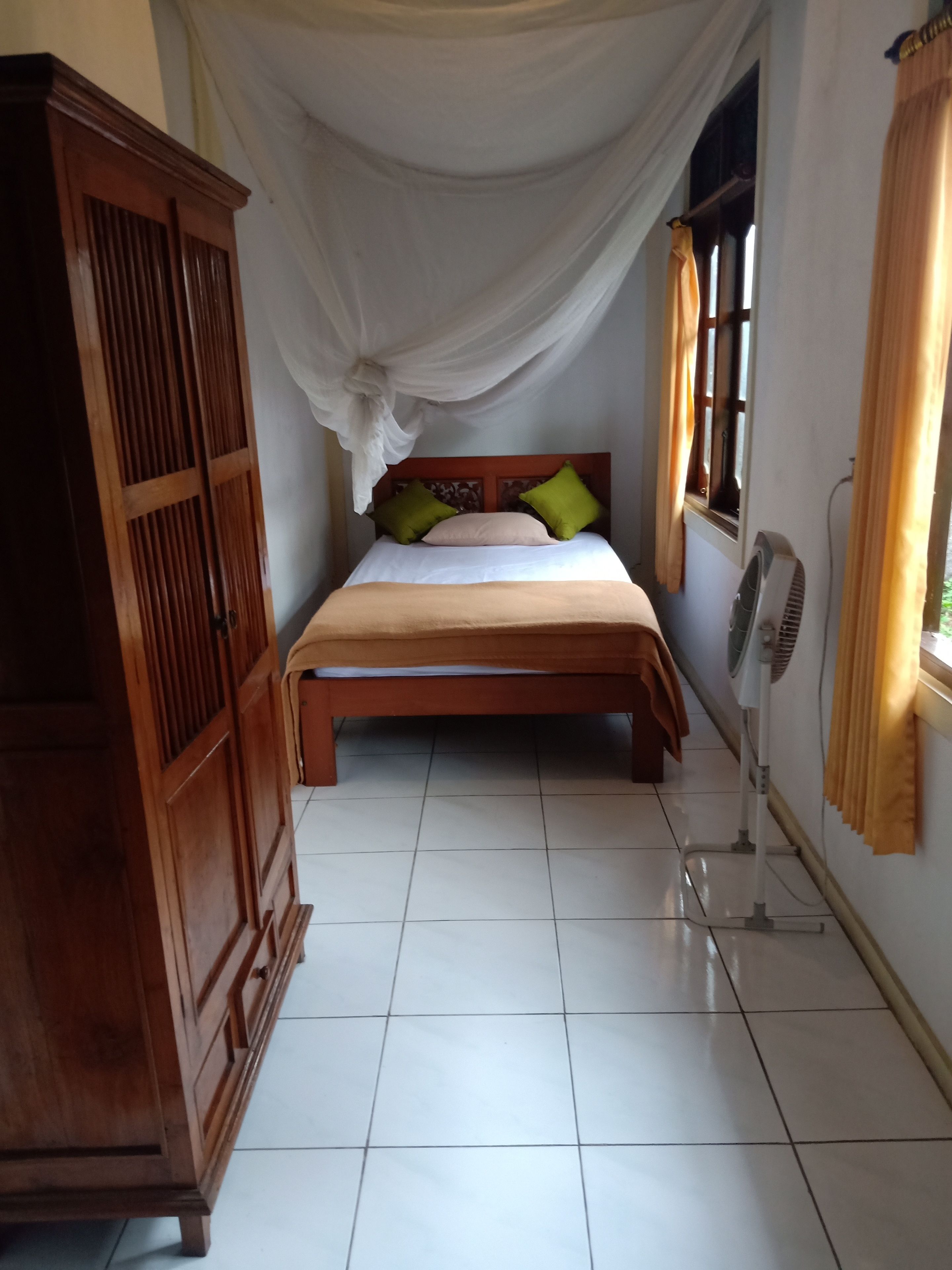 Un dormitorio con una cama, un armario de madera, un ventilador y una ventana con cortinas.