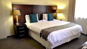 Une chambre d’hôtel avec un grand lit, deux tables de chevet avec des lampes, une tête de lit et une fenêtre avec des rideaux.
