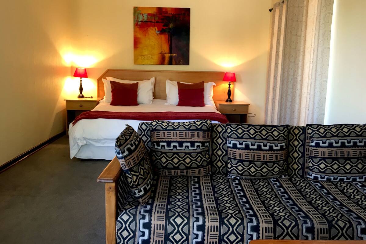 Une chambre d’hôtel avec un lit, deux tables de chevet avec des lampes, un canapé à motifs et un tableau au mur.