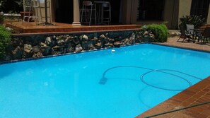 A swimming pool with a stone border, a hose, and outdoor seating. - The Bedford View Guest House (Germiston)