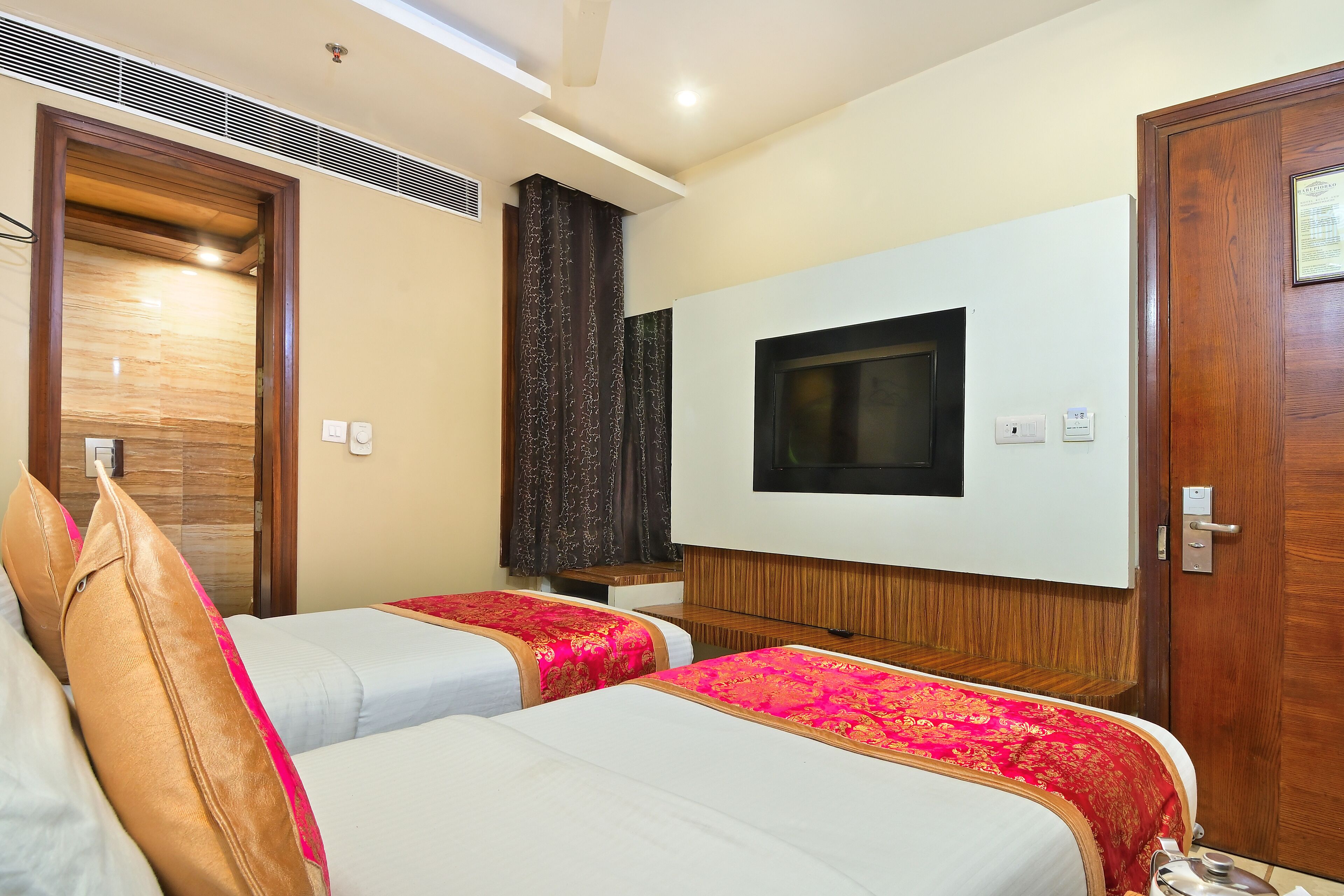 A hotel room with two beds, a TV mounted on the wall, and a wooden door.