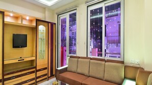 A living room with a sofa, a glass coffee table, a TV on a wooden cabinet, and large windows with city lights outside. - Hari Piorko Inn Express (New Delhi)