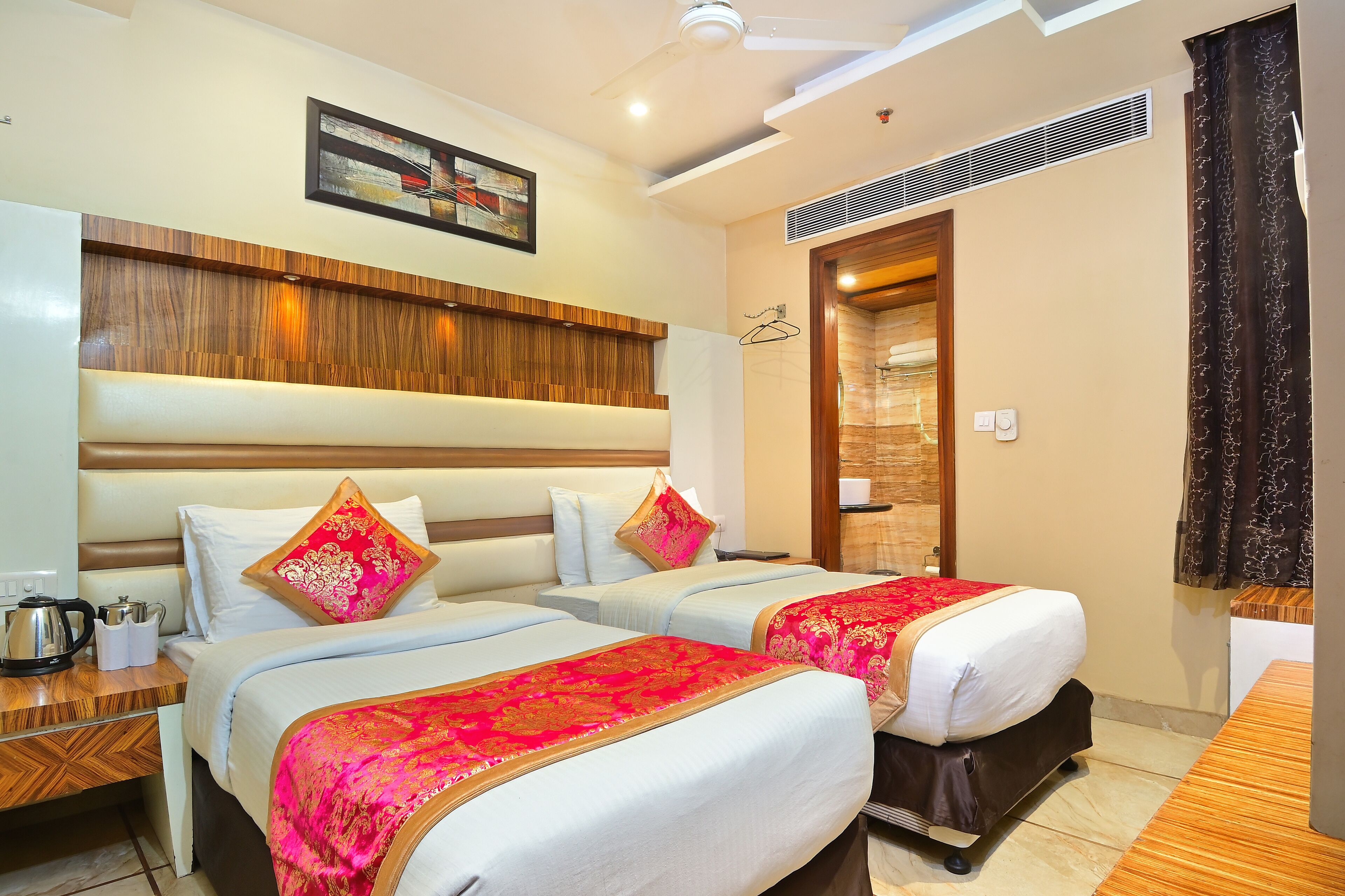 A hotel room with two beds, wooden headboards, a ceiling fan, a framed picture, and a door leading to a bathroom.