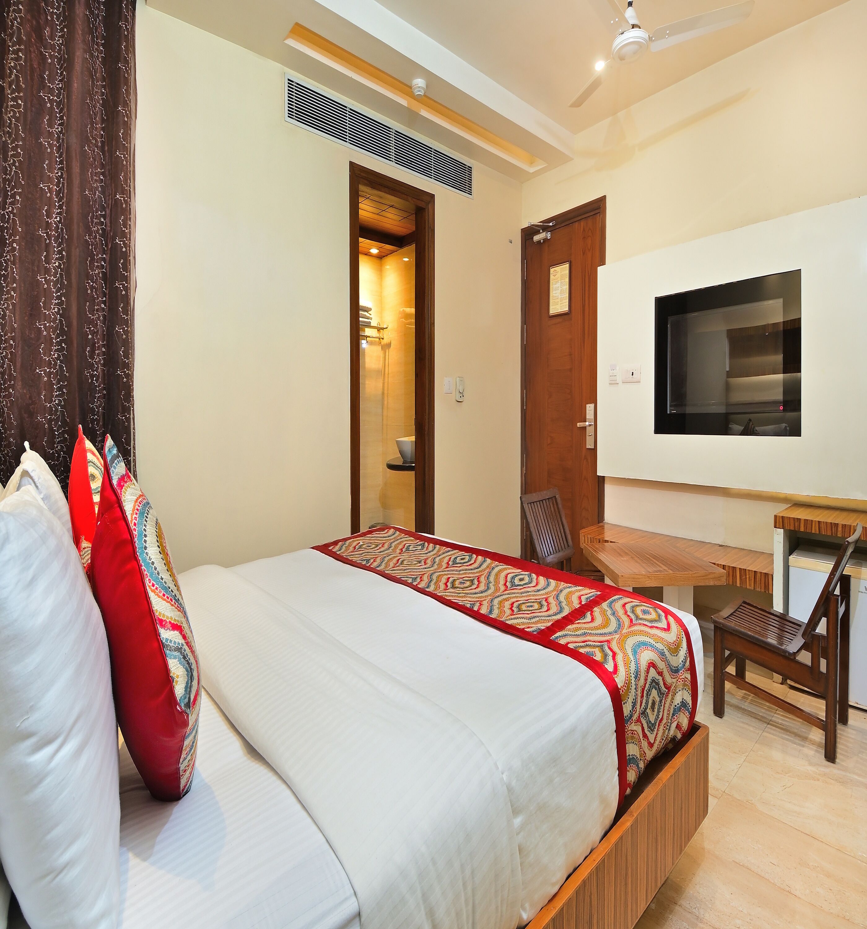 Quarto com cama, escrivaninha, cadeira, televisão e zona de chuveiro.