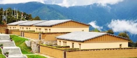 A row of traditional buildings with a stone pathway leading up to them, set against a mountainous backdrop.