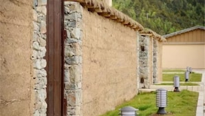 Un edificio rústico con pared de piedra y puerta de madera, rodeado por un camino con separadores decorativos.