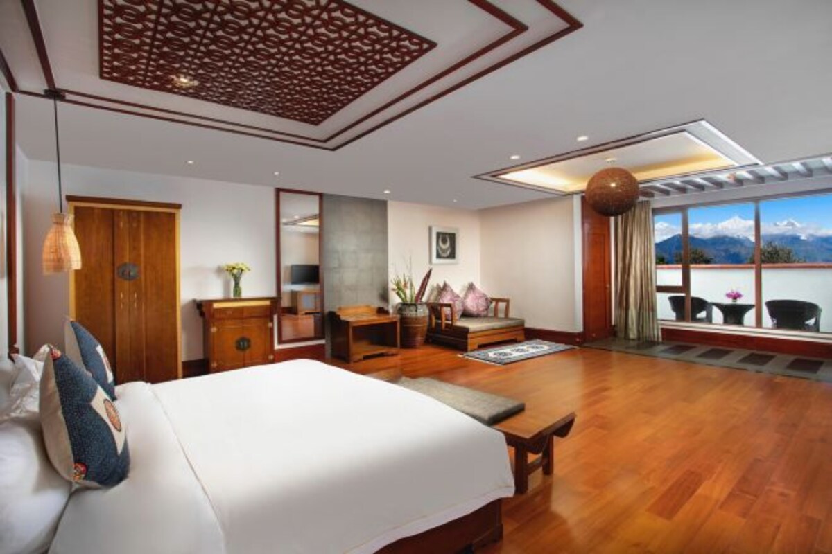 Een moderne hotelkamer met een groot bed, houten vloer, een eettafel, een zithoek en uitzicht op bergen door grote ramen.