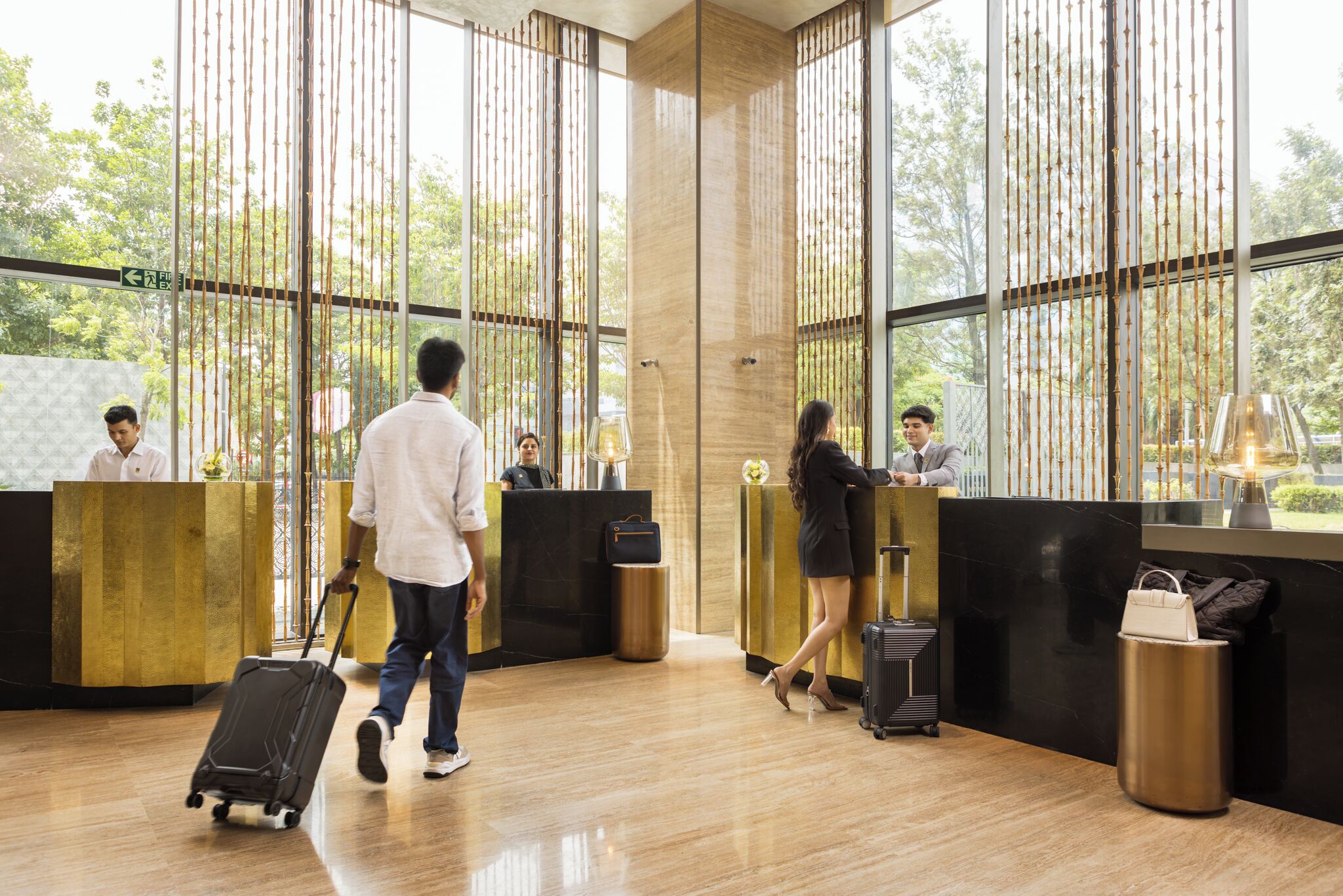 A modern reception area with wooden reception desks, a luggage trolley, and a clear view of the outdoors through large windows.