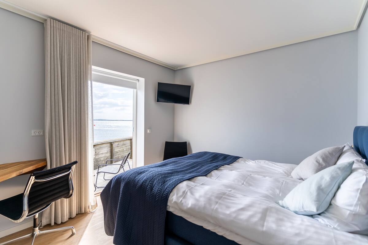 Habitación de hotel con cama, escritorio, silla, televisión y ventana con cortinas.