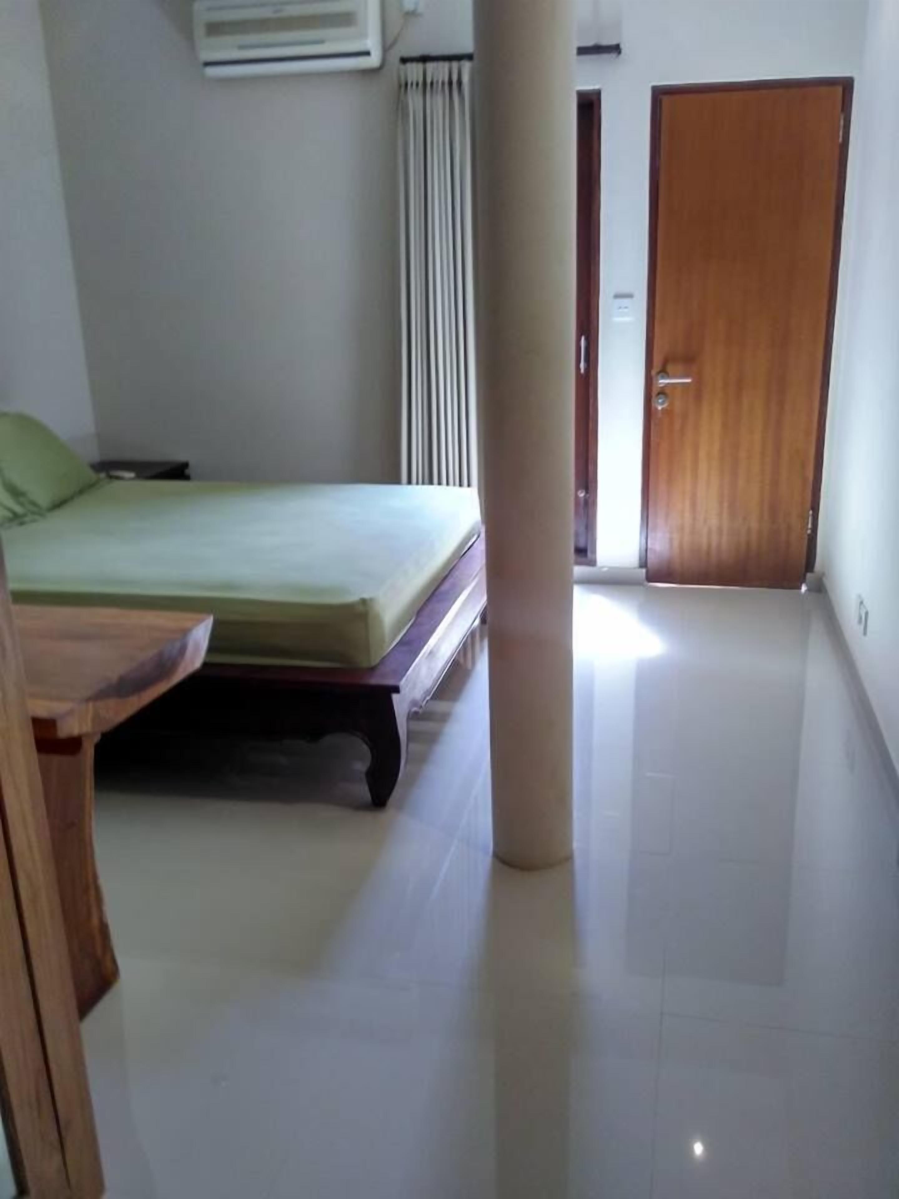 A room with a bed, a wooden table, a pillar, a door, and a window with curtains.