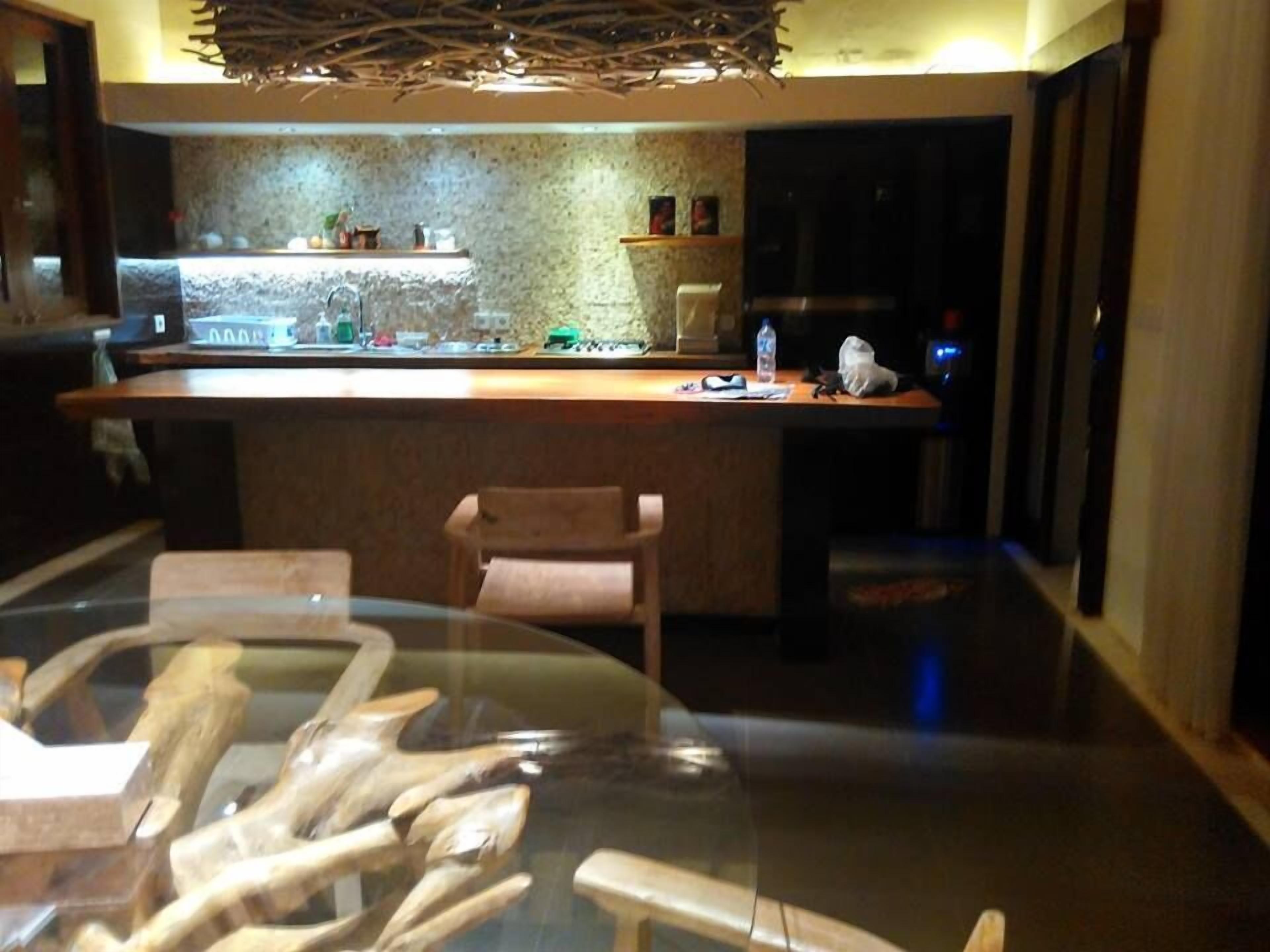 Een moderne bar met een achtergrond van een stenen muur, een houten toonbank en een glazen tafel met houten bestek.