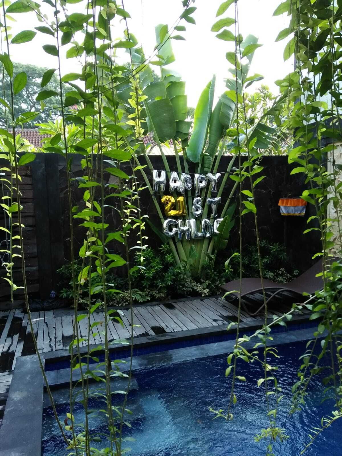 A garden with a pool, surrounded by greenery and a 'Happy 21st Birthday' balloon decoration.