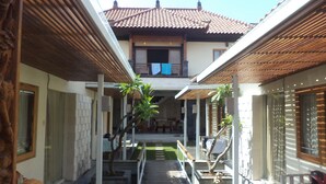 A courtyard with a wooden deck, potted plants, and a traditional tiled roof building in the background. - Intan Legian Seminyak Villa (Denpasar)