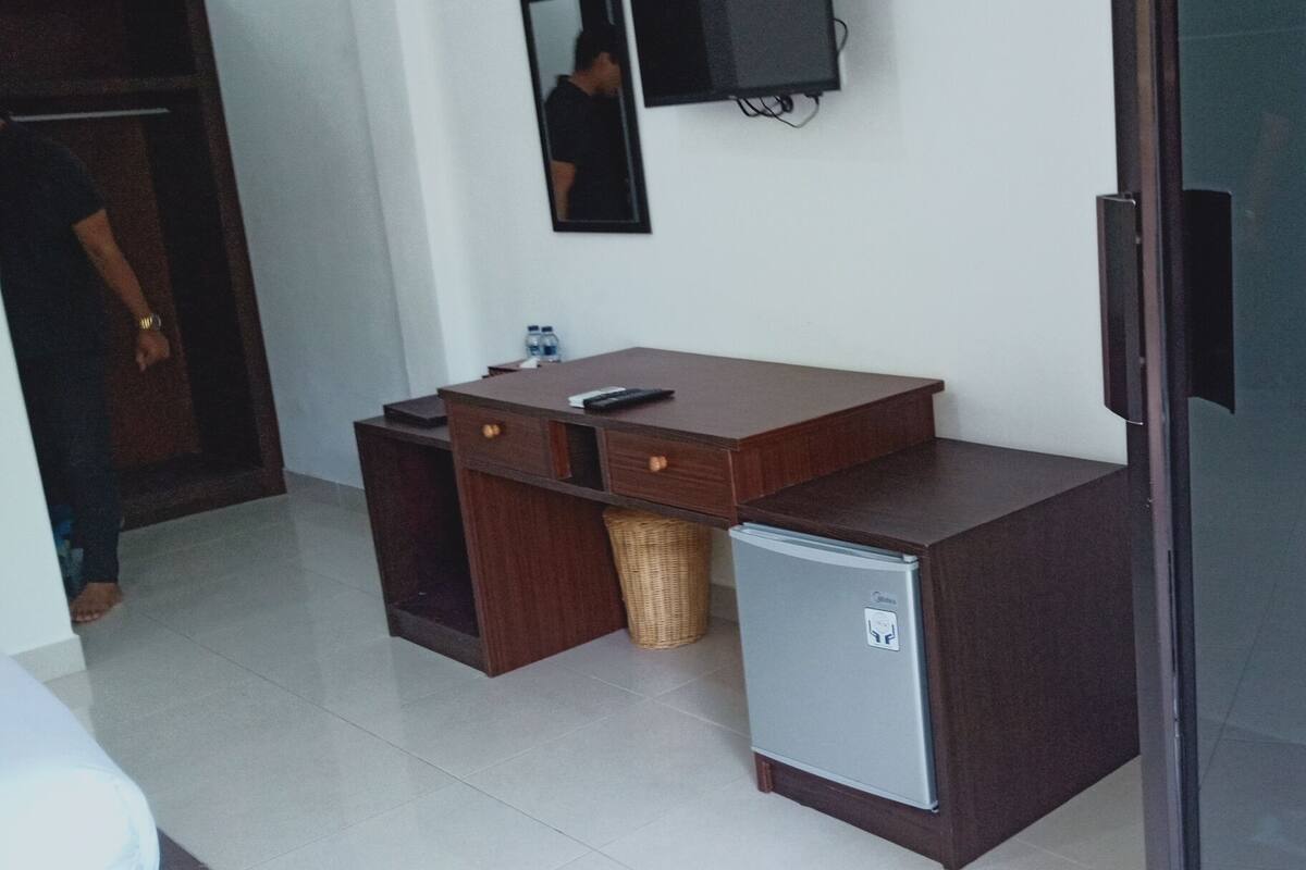 Habitación compacta con un escritorio de madera, un refrigerador pequeño, una cesta de mimbre y un televisor instalado en la pared.