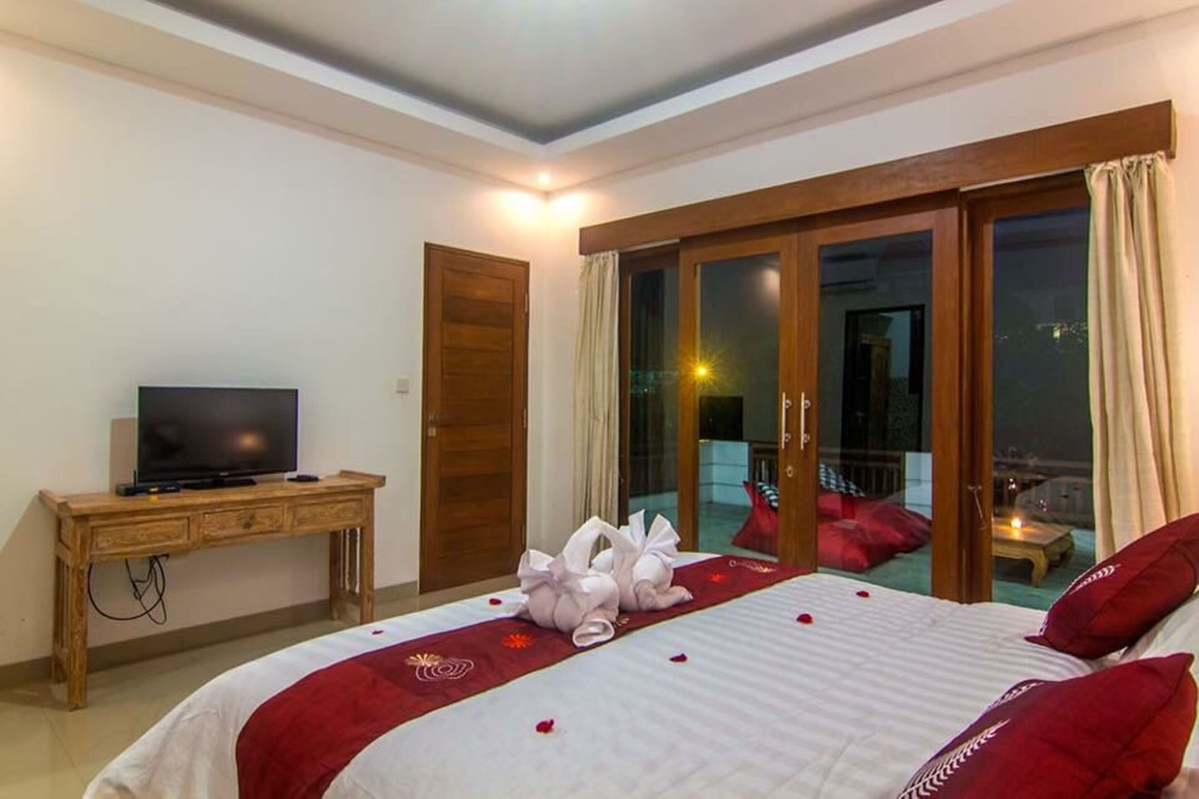 Habitación de hotel con cama, televisor, escritorio de madera y balcón con vistas.
