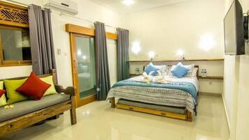 A hotel room with a bed, a sofa, a TV, and a sliding door.