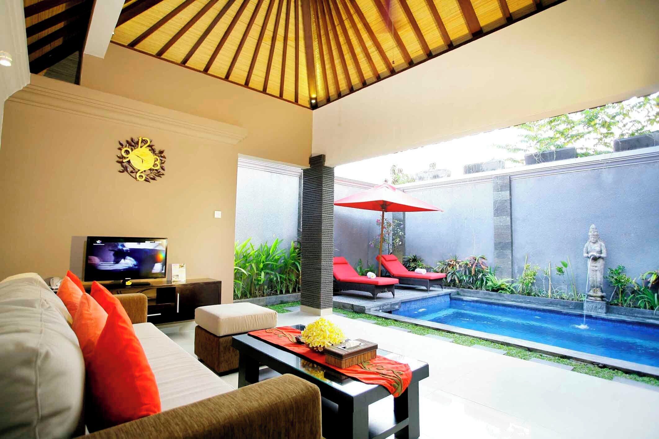 A modern living room with a TV, sofa, and a small pool area with red lounge chairs and a statue.