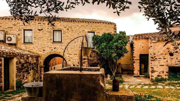Un edificio rústico de piedra con un patio, un pozo tradicional y un pequeño árbol.