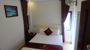 A hotel room with a bed, a nightstand, a telephone, a picture frame, and a window with curtains. - Seaside Hotel (Da Nang)