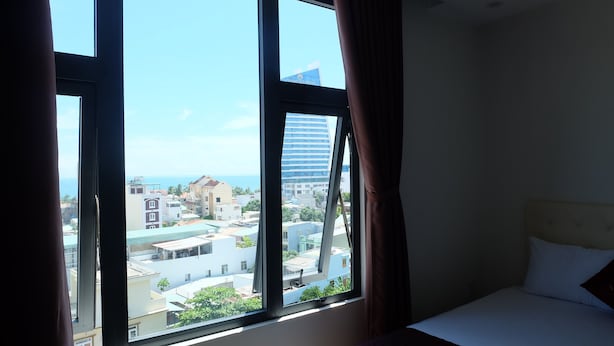 A hotel room with a large window offering a view of the cityscape and a building labeled "Grand Tourane." - Seaside Hotel (Da Nang)