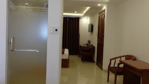 A hotel room with a wooden door, a small table with a chair, a TV mounted on the wall, and a curtain. - Seaside Hotel (Da Nang)