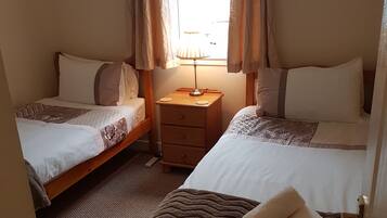 A room with two beds, a nightstand, a lamp, and a window with curtains.