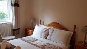A neatly made bed with a wooden headboard, a bedside table with a lamp, and a window with curtains. - Apartment 3 Pheonix Flats (Portree)